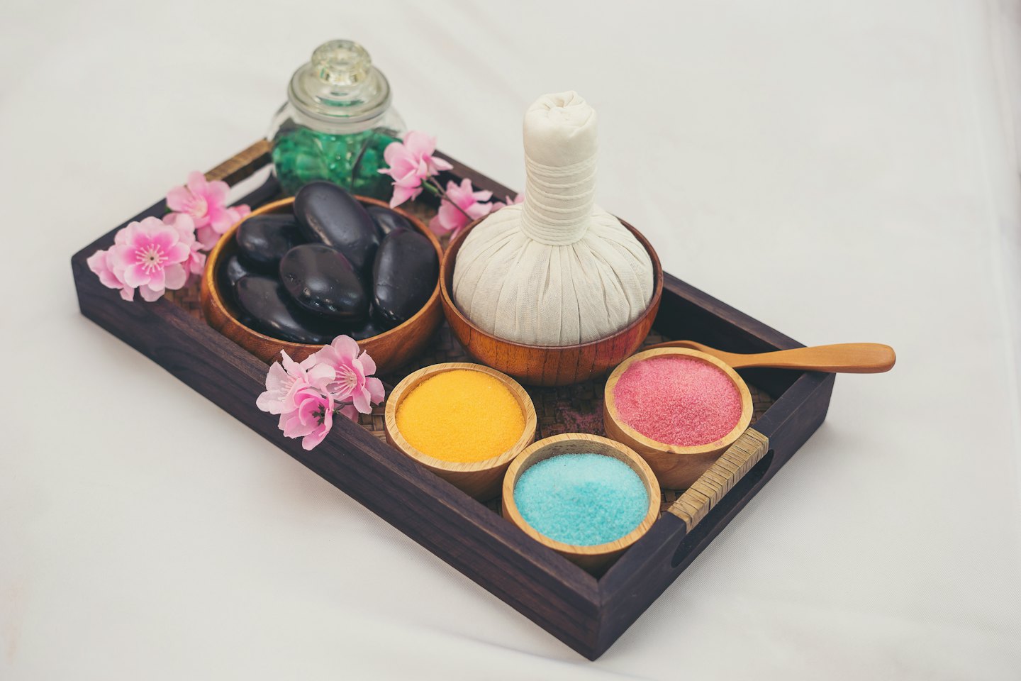 Pierres de massage et sels de bain disposés sur un plateau en bois.
